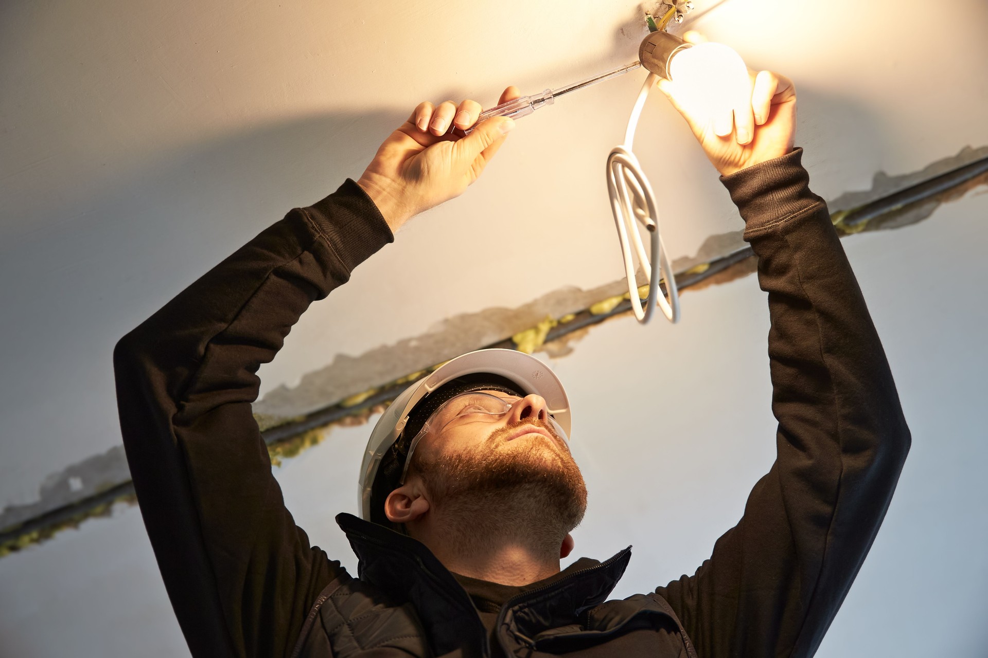 Portrait of male electrician, focused on wiring a temporary light bulb fixture.